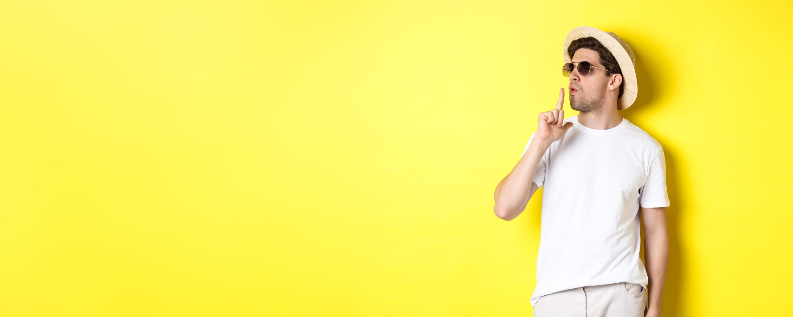 cool young male tourist blowing at finger gun and looking confident, standing against yellow background. vacation and lifestyle concept